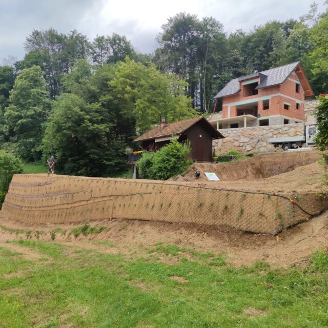 Terasirana škarpa na gradbišču hiše, v ozadju gorska koča.