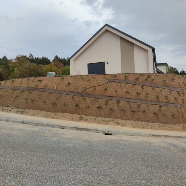 Ozelenjena škarpa s progami rastlin ob stanovanjski hiši.
