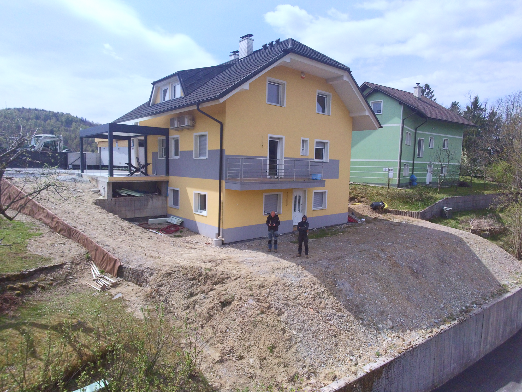 Rumeno-siva večnadstropna hiša, pred katero gradijo BVS z zemeljsko brežino.